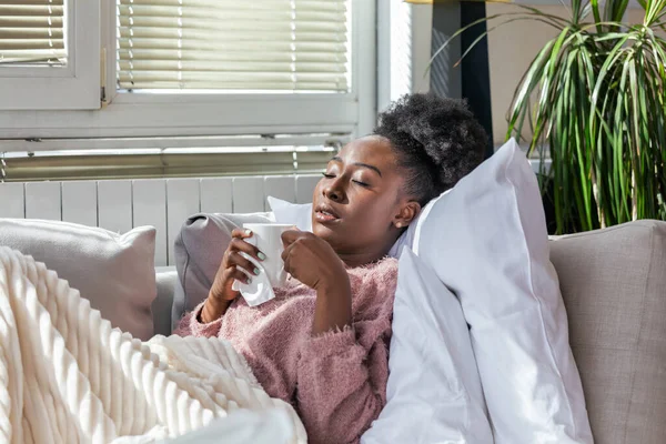 Sick African American woman with headache sitting under the blanket. Sick woman covered with a blanket lying in bed with seasonal infections, flu, allergy resting.