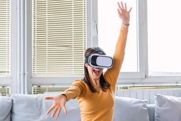 It is so real! Attractive woman adjusting her VR headset and smiling while sitting on the carpet at home. VR glasses. 360 degrees. Virtual reality headset. VR game. Wearing virtual reality goggles.