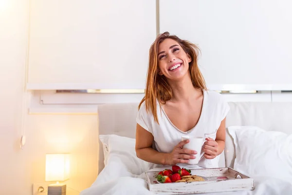 Happy attractive woman woke up in the morning in bed. Woman having breakfast in the hotel room, Woman having breakfast in bed with fruits, coffee and biscuits