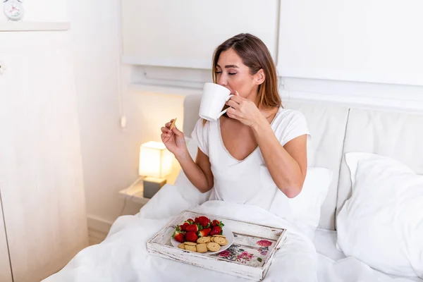 Woman having breakfast and cup of coffee in the hotel room . Tray with breakfast on a bed for lovely beautiful girl. Beautiful woman laying and enjoying, breakfast in bed