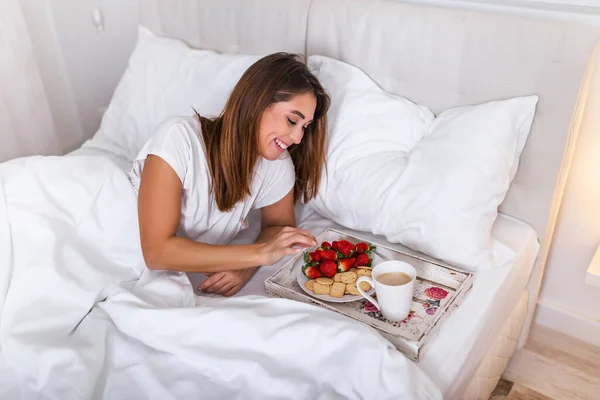 Woman having breakfast in the hotel room . Tray with breakfast on a bed for lovely beautiful girl. Beautiful woman laying and enjoying, breakfast in bed