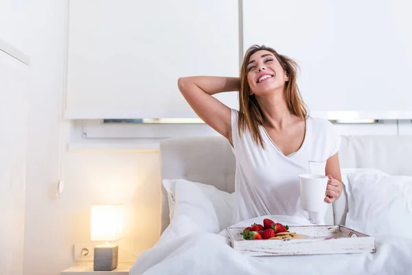 attractive woman in pajamas waking up in the morning with the smell of coffee and fresh breakfast on wooden tray in bed