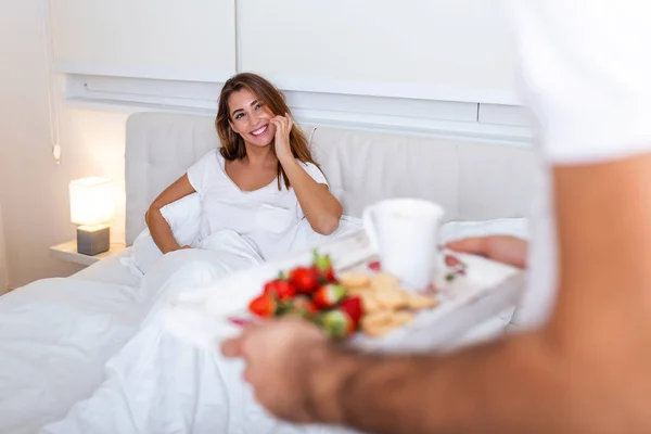 Care and romance at the morning. Surprised and happy young woman lying at the bed with male hands bringing breakfast. Good morning Healthy breakfast in bed.