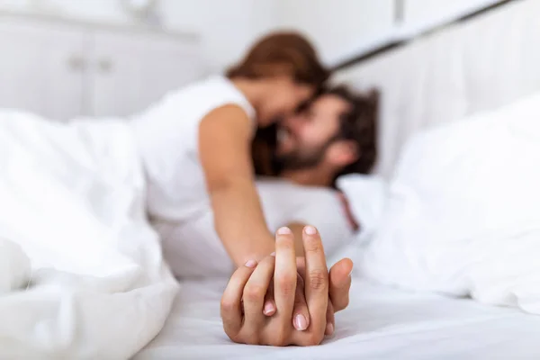 Romantic couple in bed enjoying sensual foreplay. Focus on hands man and woman. Happy sensual young couple lying in bed together. Beautiful loving couple kissing in bed.