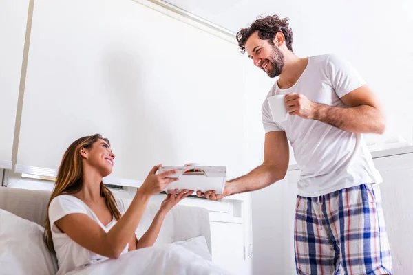 Good morning! Healthy breakfast in bed. Beautiful young woman is lying in bed while her handsome man bringing tasty breakfast.