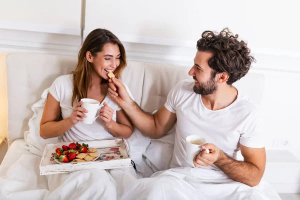 Young handsome man feeding attractive young woman in bed in the morning. Romantic breakfast for two. Love , care, relatioships. couple having healthy breakfast together in bed at home