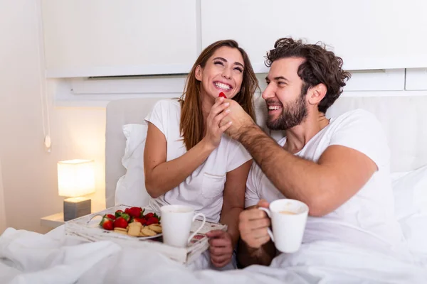 Couple in love having breakfast in bed. Young caucasian couple having romantic breakfast in bed. Female and male , two cups of coffee, fruits and colorful biscuits.