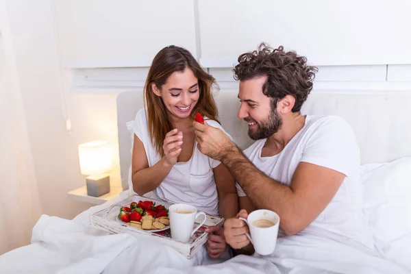 Couple in love having breakfast in bed. Young caucasian couple having romantic breakfast in bed. Female and male , two cups of coffee, fruits and colorful biscuits.