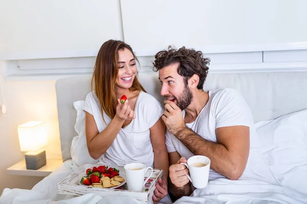 Young married couple in love eating breakfast in their bed. Good morning! Healthy breakfast in bed. Young beautiful love couple is having breakfast in bed.