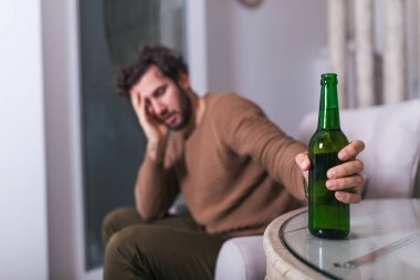 İşten sonra depresif bir adam kanepede oturmuş, soğuk bir bira içiyor. Bardak tutan adam, evde tek başına içen adam. alkolizm, alkol bağımlılığı ve insanlar konsepti