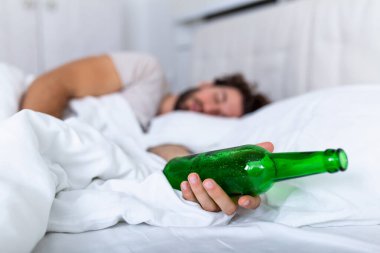 Elinde bir şişe alkolle bilinçsiz sarhoş bir adam yatakta uyuyor. Alkolizm sorunu ve akşamdan kalma konsepti