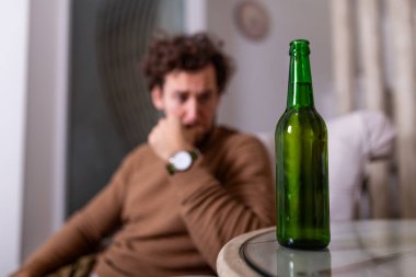 Alkolik adam bira şişesine uzanıyor, adam evde tek başına içiyor. Alkolizm, alkol bağımlılığı ve insan konsepti. Evde tek başına bira içen erkek alkolik.