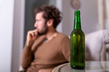 Alkol şişesinin arkasında içki içen isimsiz alkoliğin silueti. Alkol alışkanlıklarıyla kavga eden bir adam, evde kanepede oturup içki içen bir adam.