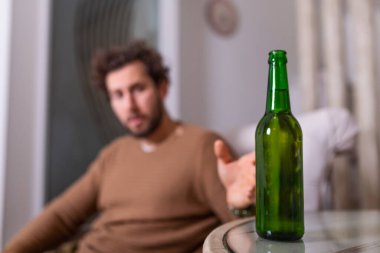 Alkolik adam bira şişesine uzanıyor, adam evde tek başına içiyor. Alkolizm, alkol bağımlılığı ve insan konsepti. Evde tek başına bira içen erkek alkolik.