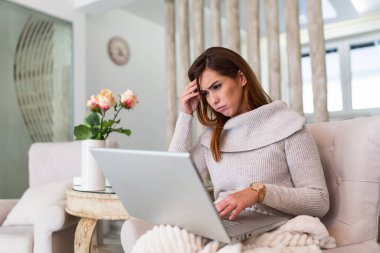 Genç, dizüstü bilgisayarda oturup endişe dolu bir ifadeyle ekrana bakarak bağımsız çalışmanın stresini yaşıyor. İş ve serbest meslek kavramı. Tasarımcı kadın evde dizüstü bilgisayarın önünde oturuyor..