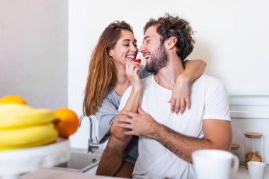 Güzel genç çift birbirlerini besliyor ve evde yemek pişirirken gülümsüyor. Mutlu sportif çift hafif mutfakta sağlıklı yiyecekler hazırlıyor. Sağlıklı gıda konsepti.