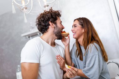 Güzel, genç bir çift birbirlerine bakıyor ve mutfakta yemek pişirirken birbirlerine gülümsüyorlar. Sevgi dolu genç bir çift. Sarılmak ve yemek yapmak. Mutfakta eğlenmek.