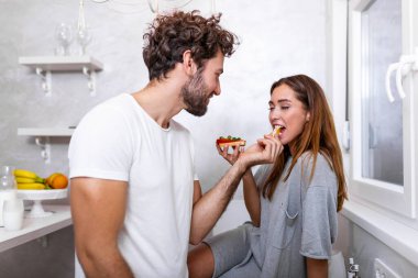 Güzel, genç bir çift birbirlerine bakıyor ve mutfakta yemek pişirirken birbirlerine gülümsüyorlar. Sevgi dolu genç bir çift. Sarılmak ve yemek yapmak. Mutfakta eğlenmek.