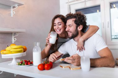 Mutlu genç çift, taze meyve ve sebze salatası hazırlarken modern mutfakta eğleniyor. Güzel, genç bir çift mutfakta sağlıklı yemekler pişirirken konuşuyor ve gülümsüyor..