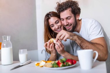 Güzel, genç bir çift birbirlerine bakıyor ve mutfakta yemek pişirirken birbirlerine gülümsüyorlar. Sevgi dolu genç bir çift. Sarılmak ve yemek yapmak. Mutfakta eğlenmek.