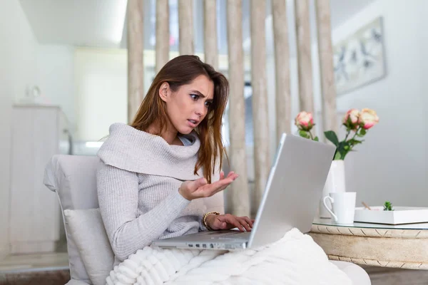 Attractive mad woman sitting at her sofa at home, looking at laptop screen with angry expression. Too much workload, file error, all data failed, forgot to save document
