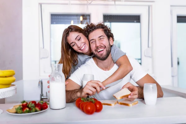 Romantic young couple cooking together in the kitchen,having a great time together. Man and woman laughing and drinking milk in the morning with breakfast