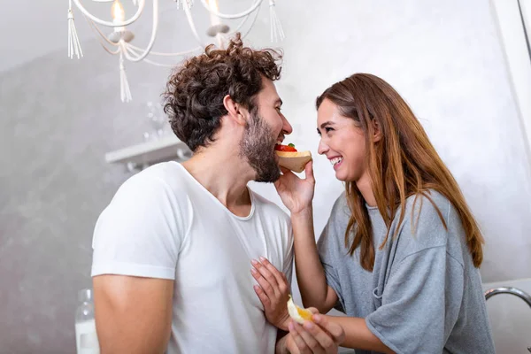 Güzel, genç bir çift birbirlerine bakıyor ve mutfakta yemek pişirirken birbirlerine gülümsüyorlar. Sevgi dolu genç bir çift. Sarılmak ve yemek yapmak. Mutfakta eğlenmek.