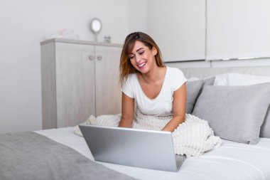 Evdeki yatakta dizüstü bilgisayarla çalışan mutlu, sıradan bir kadın. Evde dizüstü bilgisayarıyla çalışan serbest çalışan bir kadın.