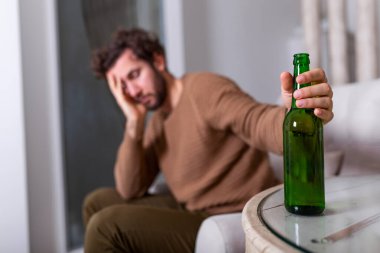 Alkolik adam bira şişesine uzanıyor, adam evde tek başına içiyor. Alkolizm, alkol bağımlılığı ve insan konsepti. Evde tek başına bira içen erkek alkolik.