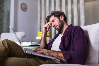 Evde dizüstü bilgisayar başında çalışan yorgun işadamı, burun köprüsüne masaj yapıyor, yorgunluk hissi veriyor, evde baş ağrısı çeken yakışıklı genç adam, yakın çekim.