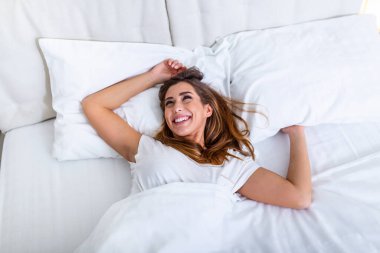 Güzel bir kadın yatağında uyanıyor, gülümsüyor ve esniyor. Genç ve güzel bir kadın yatağında tamamen dinlenmiş olarak uyanıyor. Uyandıktan sonra yatakta gerinen bir kadın. Sağlıklı bir yaşam tarzı. Refah kavramı