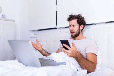 Yatakta sinirli bir adam online kötü haber yüzünden ya da bilgisayar yazılımı hatası yüzünden kızgın, deli çaresiz bir adam bozuk dizüstü bilgisayarla sorun yaşıyor, sabahları evden çalışıyor ve kahve içiyor.