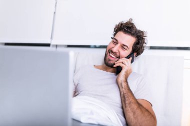 Kafkasyalı genç bir adamın sabah kahvesini içtiği, yatağında oturduğu, laptopuyla çalıştığı ve cep telefonuyla konuştuğu incelenmeye hazırlandığı, internette sörf yapmak için dizüstü bilgisayar kullandığı görüntüsü..