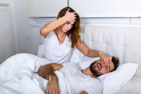 Couple in bed, man snoring and woman can't sleep. Snoring man and young woman. Couple sleeping in bed. Young girl can't sleep because of her man's snoring holding his nose. Snoring man problem