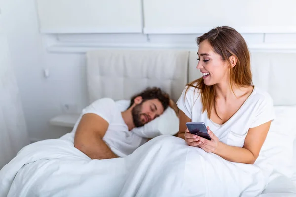 Cheating wife. Beautiful woman chatting privately on cellphone, hiding from her sleeping husband, empty space. Cheating Girlfriend Chatting On Phone While Boyfriend Sleeping In Bedroom At Night.