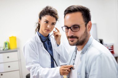 Genç bayan doktor, klinikte steteskoplu erkek kalp göğsünü dinliyor. Kadın pratisyen hekim, erkek hastayı fonendoskopla muayene ediyor. sağlık hizmeti kavramı.