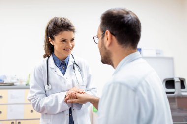 Genç bayan doktor, beyaz bir hastanın elini tutuyor. Rahatlık veriyor, sağlık sigortası sempati gösteriyor, sağlık yardımı alıyor ve tıbbi yardım alıyor. Tıbbi muayenede kısır hastaları rahatlatmaya çalışıyor.