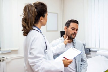 İlaç, sağlık ve sağlık muayenesi konsepti - hastanede hastanın bademciklerini kontrol eden doktor ya da hemşire. Endokrinolog klinikte genç bir adamın boğazını inceliyor.