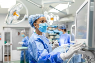 Ameliyathanede çalışan anestezi uzmanı koruyucu giysi giyerek hastaya hastanede ameliyat öncesi sakinleştirici verirken monitörleri kontrol ediyor.
