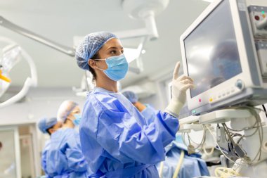 Ameliyat öncesi anestezi makinesi hazırlayan önlüklü ve koruyucu maskeli genç bir kadın doktor portresi.