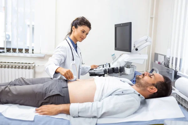 Ultrasound diagnostic of stomach on abdominal to man in clinic, closeup view. Doctor runs ultrasound sensor over patient\'s tummy and looks at image on screen. Diagnosis of internal organs.