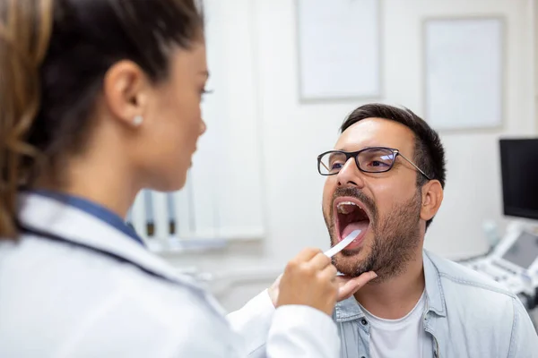 医者が喉を見るために口を開ける男性患者 診療所で患者の喉の痛みを調べる女性医師 耳鼻咽喉科医は患者の喉の痛みを調べる — ストック写真