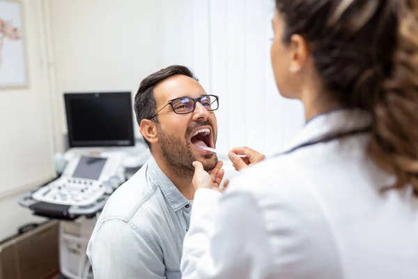 Doctor using inspection spatula to examine patient throat. ENT doctor doing throat exam. patient opened his mouth to throat check-up