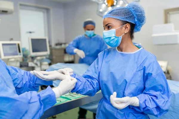 Νεαρή Νοσοκόμα Προστατευτική Μάσκα Και Ενδύματα Εργασίας Που Βοηθούν Χειρουργό — Φωτογραφία Αρχείου