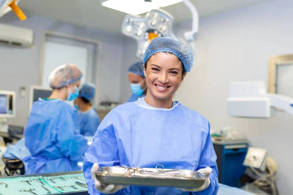 Portrait of female woman nurse surgeon OR staff member dressed in surgical scrubs gown mask and hair net in hospital operating room theater making eye contact smiling pleased happy looking at camera