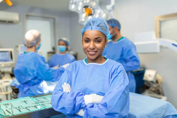 Close-up of a African American surgeon woman looking at camera with colleagues performing in background in operation room. The concept of medicine