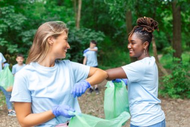 Çöpten gönüllü grup parkı temizliyor. Genç kadın ve erkekler ormanda yürürken ellerinde plastik poşetlerle. Açık hava temizlik kavramı