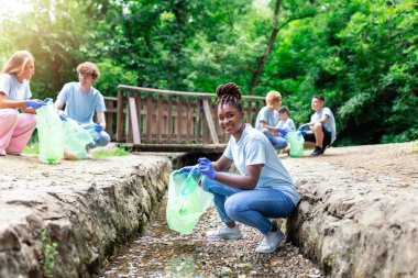 Doğa temizliği, gönüllü ekoloji yeşil kavramı. Genç bir kadın gün batımında nehri alır. Çevre plastik kirliliği. Koruyucu eldivenli bir kadının ev atıklarını torbaya koyarkenki görüntüsü.