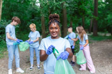 Bir grup genç arkadaş ormanda çöp torbalarına plastik şişe toplamak için gönüllü oluyor. Ekoloji kavramı