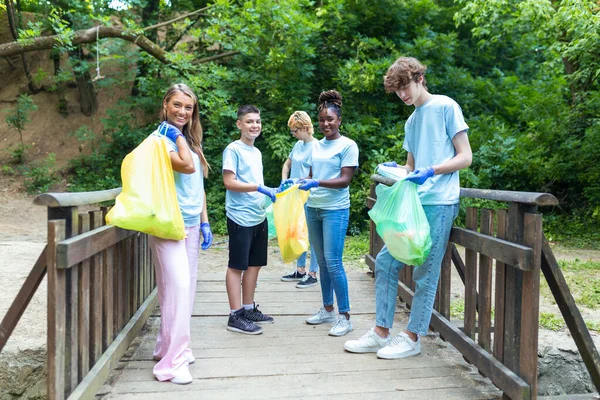 Standing in a natural parkland and holding full garbage bags, volunteers are standing looking at the camera, showing the results of their environmental clean-up
